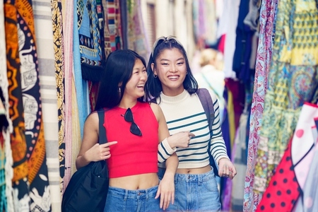 Two Asian female tourists shopping clothes in street bazaar