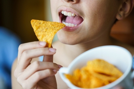 Unrecognizable girl about to eat spicy tortilla chip at home