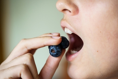 Crop anonymous girl with mouth open eating delicious blueberries