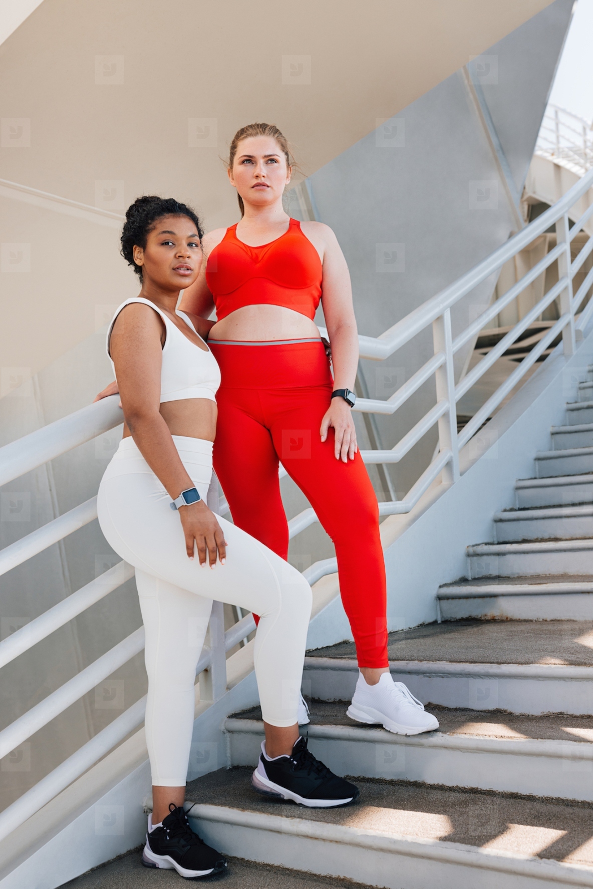 Full length of two plus size females standing on stairs outdoors  Two young women in sportswear are looking away while taking a break during workout