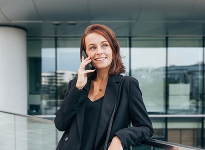 Confident woman with ginger hair making phone call outdoors  Smiling female with ginger hair in black formal wear