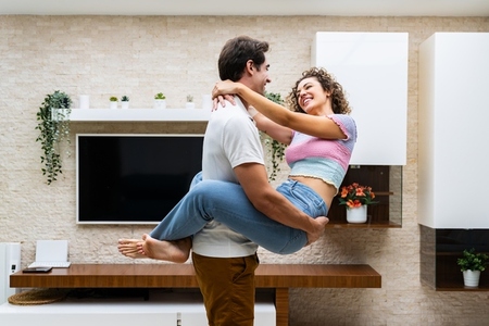 Smiling young couple embracing at home near TV on wall