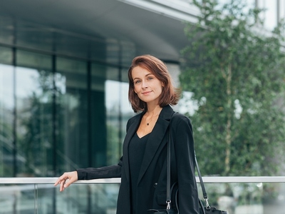 Middle aged female with ginger hair leaning railing a business building  wearing black formal clothes