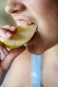 Crop teenage girl biting fresh juicy apple slice at home