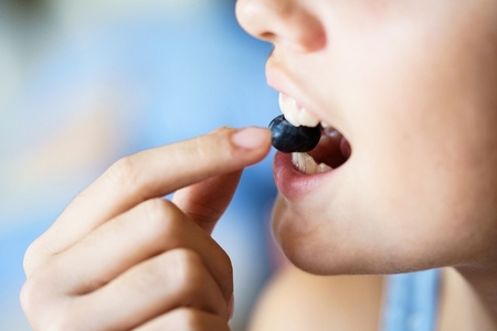 Unrecognizable girl biting fresh organic blueberry at home