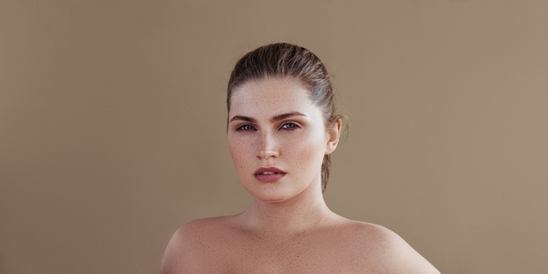 Portrait of a plus size woman posing over pastel backdrop  Young female with smooth skin looking at camera