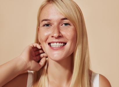 Young happy female with blond hair looking at camera in a studio  Beautiful smiling woman with freckles adjusting her hair over a beige backdrop