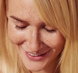 Close up of smiling blond female with freckles looking down  Highly detailed close up shot of a young female with smooth freckled skin