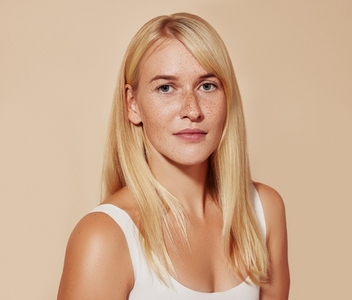 Studio portrait of a young beautiful woman with blond hair over a pastel backdrop  Female with freckled perfect skin looking at camera against a beige backdrop