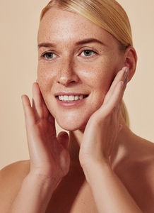 Highly detailed portrait of a young smiling woman massaging her face  Close up of blond female touching her freckled skin