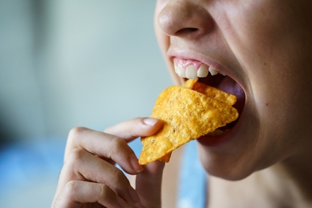 Crop anonymous girl with mouth wide open eating spicy nacho chips