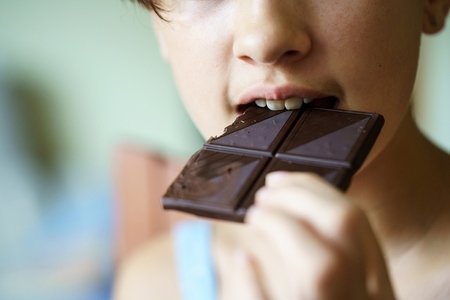 Unrecognizable girl eating delicious chocolate bar at home