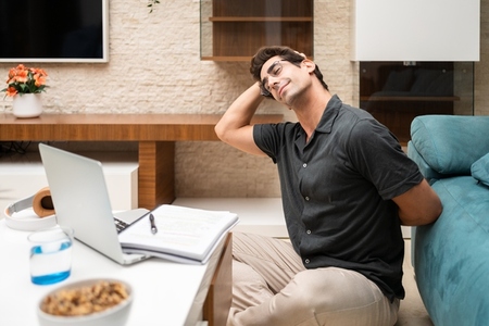 Positive man stretching neck near netbook at home