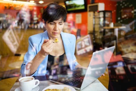 Focused woman using laptop while eating in cafe
