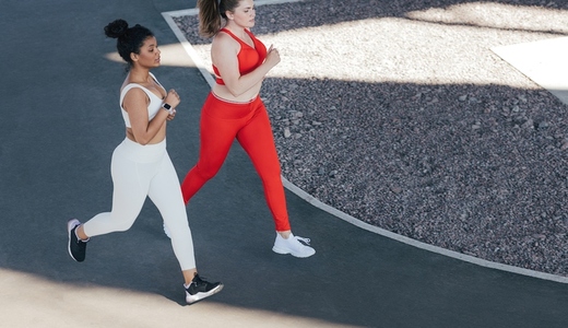 Shot from above of two females running together outdoors  High angle of two female friends jogging together wearing sportswear in different colors