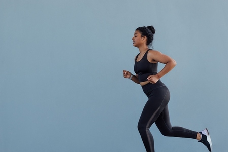 Side view of young female running at a grey wall  Woman in black fitness wear jogging outdoors