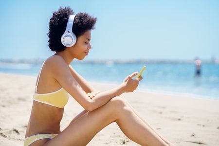 Young ethnic lady with smartphone listening to song on seashore during vacation