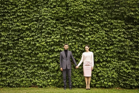 Couple Holding Hands Standing in front of Green Leafy Hedge