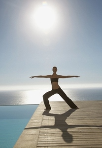 Young woman practicing yoga by a swimming pool with ocean in the background