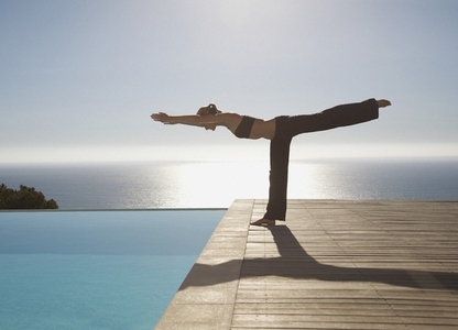 Young woman practicing yoga by a swimming pool with ocean in the background
