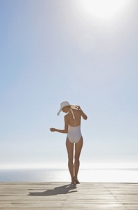 Woman in white hat and swimsuit dancing on a sun deck
