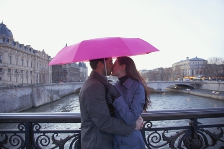Couple kissing under a pink umbrella on a bridge over the Seine rive