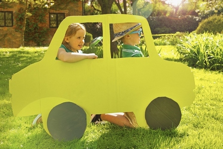 Boy and Girl Kneeling behind Cardboard Cut Out in Shape of Car