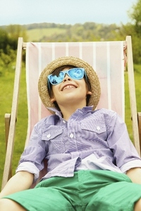 Smiling Boy Wearing Straw Hat and Sunglasses Sitting on Deck Chair