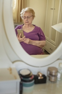 Reflection in mirror of senior woman using smart phone at home
