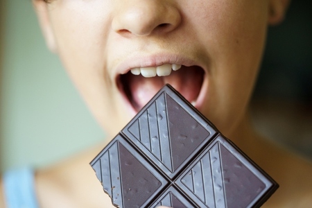 Anonymous teenage girl with mouth wide open eating chocolate bar