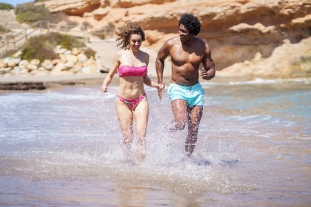Happy diverse couple jogging in sea water