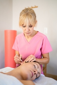 Professional beautician applying ear probe on female client in salon during auriculotherapy