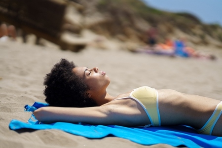 Peaceful fit ethnic lady sunbathing on seashore with closed eyes