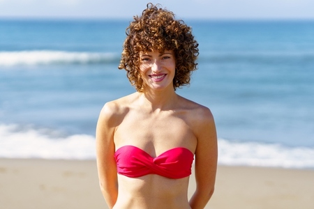 Cheerful woman in bikini on beach during sunny day