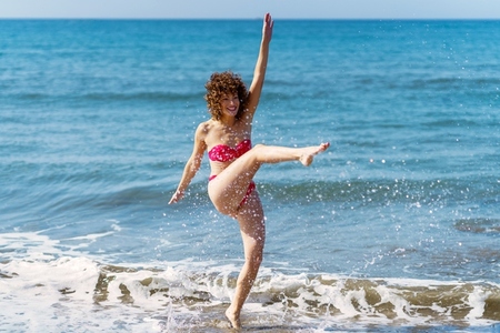 Carefree woman splashing ocean water on beach