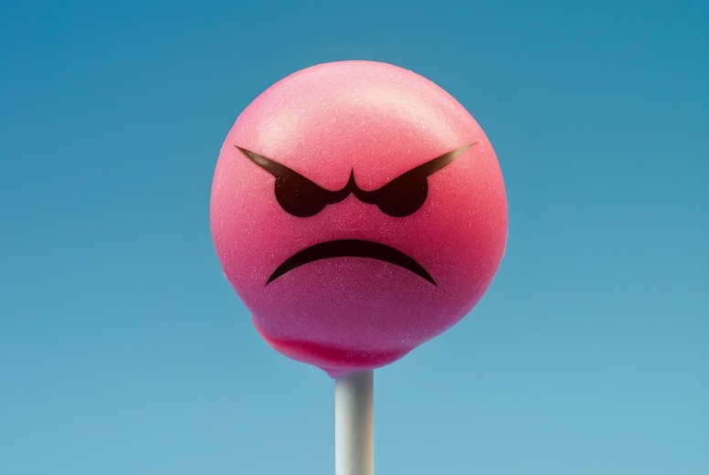 Lollipop in the shape of an angry emoji on a blue background.