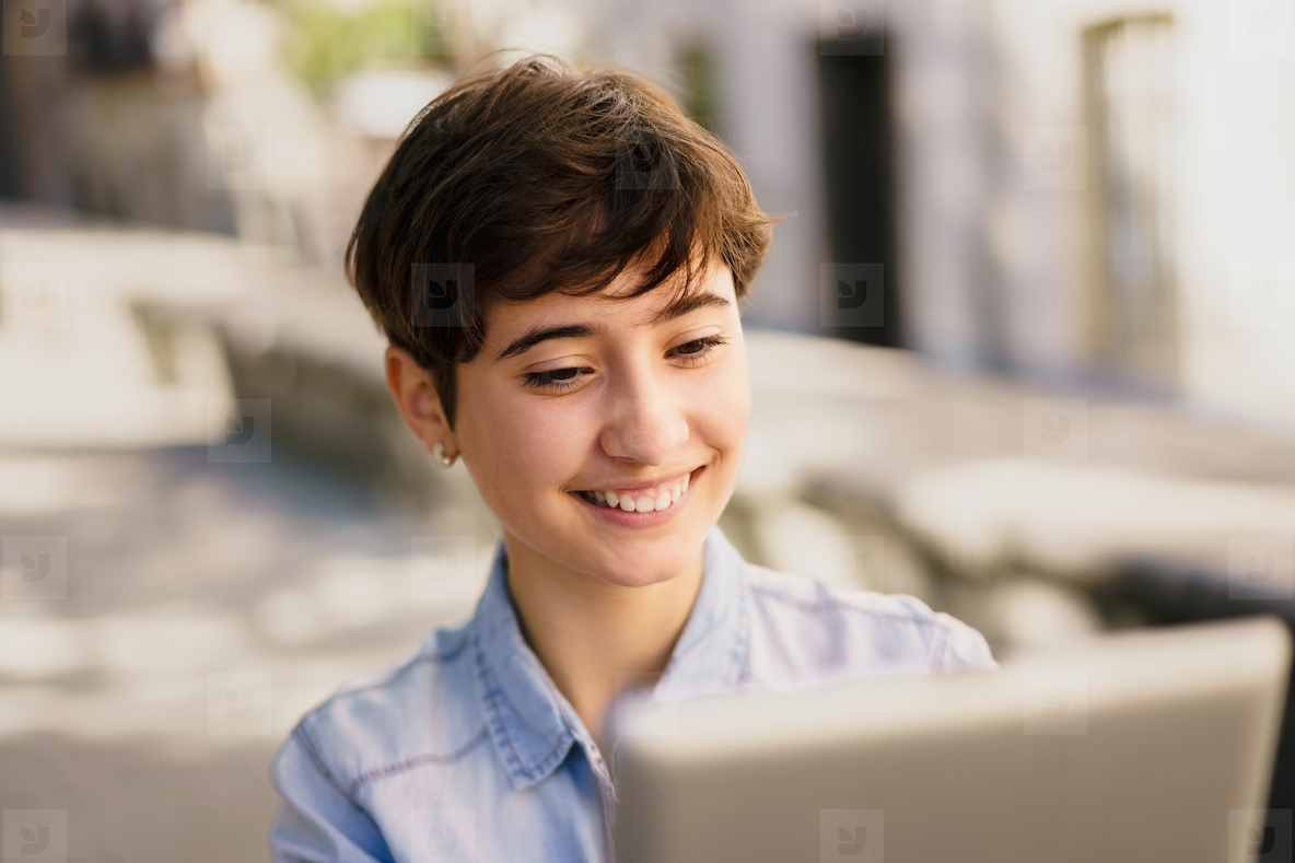 A Young Woman Brightly Smiling While Working on a Laptop in a Beautiful Outdoor Setting