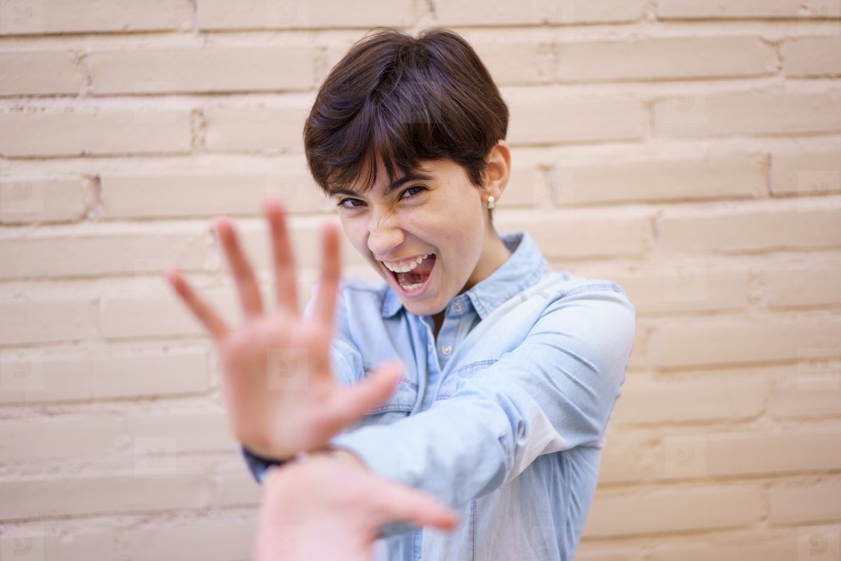 A Joyful and Cheerful Young Woman Playfully Posing Against a Colorful Brick Wall