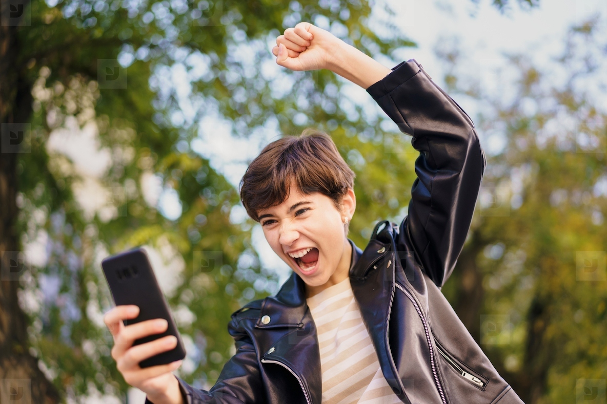 An Excited Young Individual Joyfully Celebrating with a Smartphone While in the Park