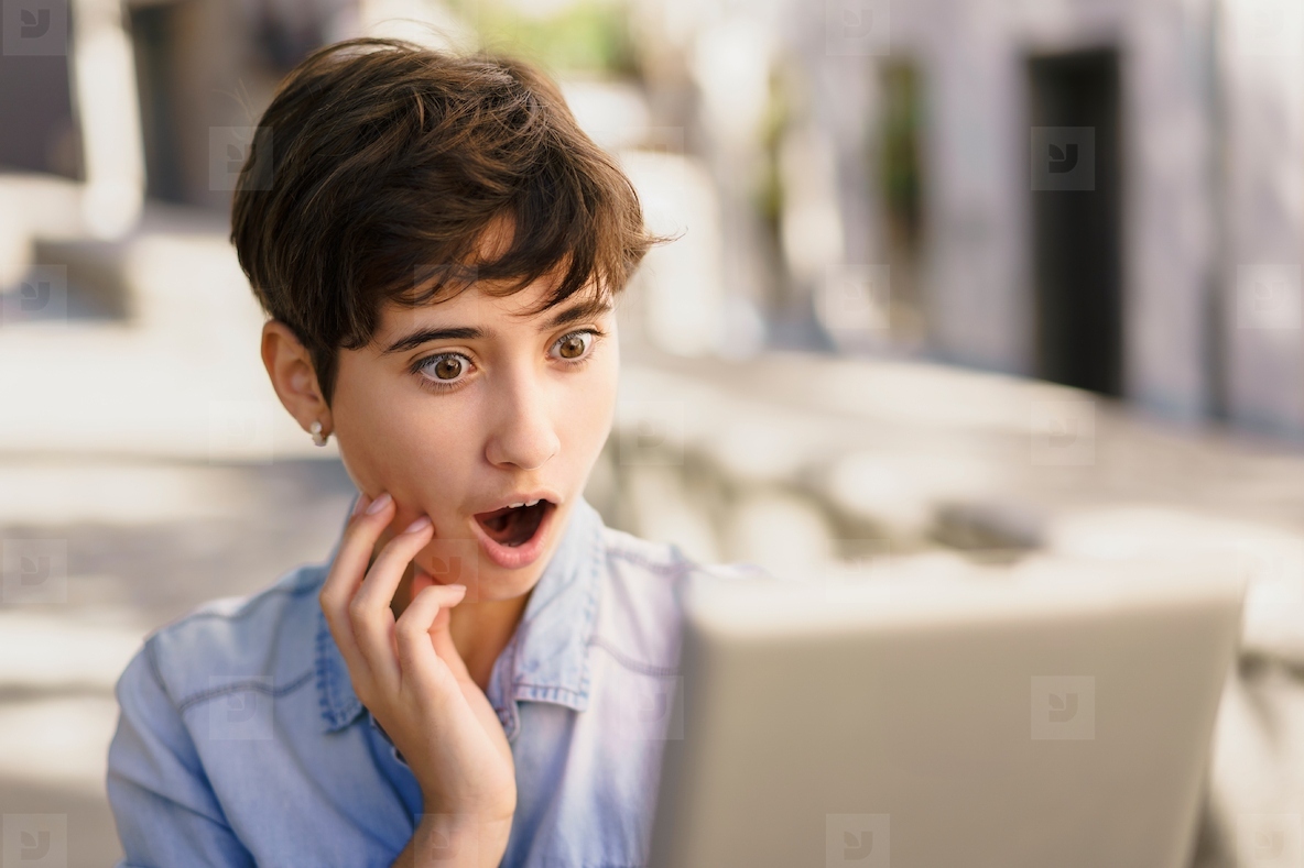 A Young Woman Looks Surprised and Reacts While Viewing Her Laptop Screen Outdoors