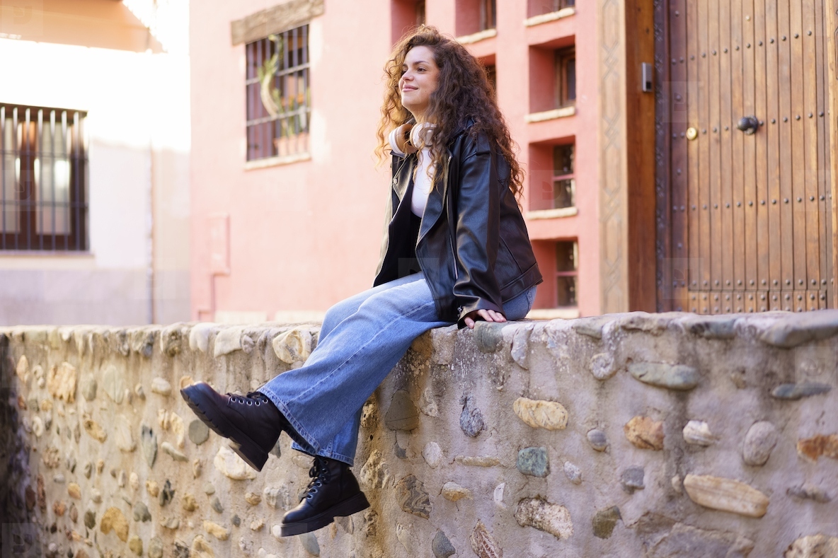 A Young Woman is Comfortably Sitting and Relaxing on a Stone Wall in a Lovely Urban Setting