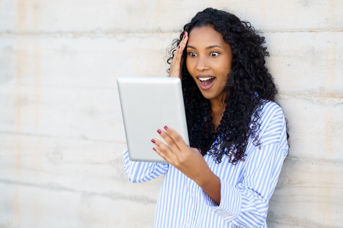 An Excited Womans Reaction while Engaging with a Tablet up against a Concrete Wall