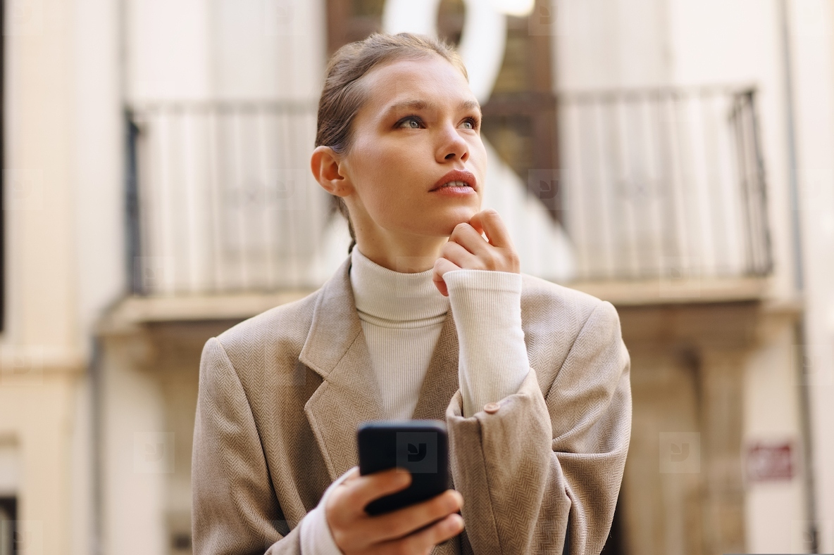 A Young Woman Deep in Thought as She Engages with Her Smartphone in a Bustling Urban Setting