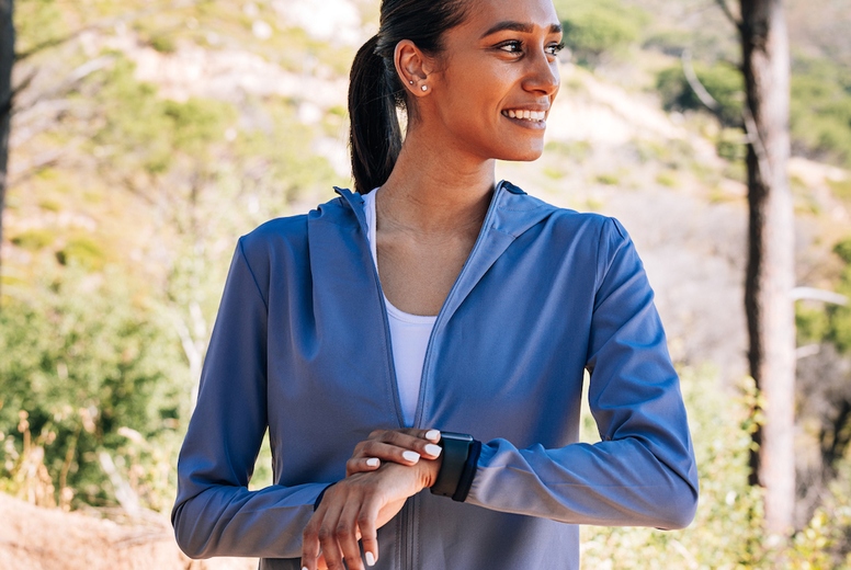 Side view of cheerful woman athlete looking away. Smiling female checking smartwatch outdoors.
