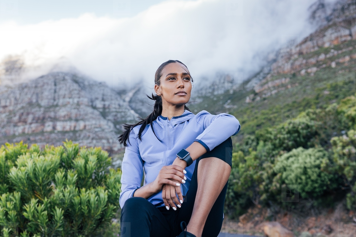 Confident slim female sitting against the stunning view in a natural park Young woman in sportswear relaxing outdoors and looking away