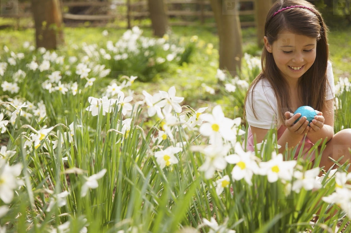 Young girl holding an Easter egg in a field of daffodils