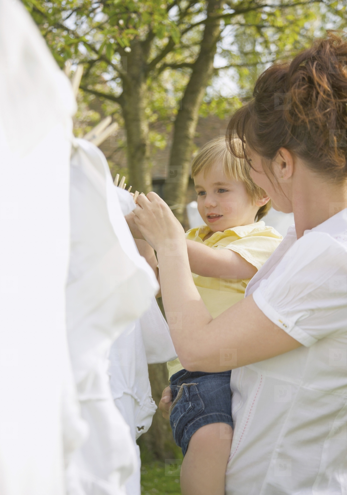 Young boy helping mother hanging linens on a clothesline