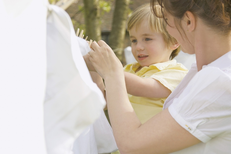 Young boy helping mother hanging linens on a clothesline