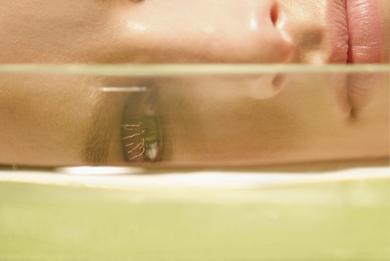 Close up of a young woman face lying behind a glass container
