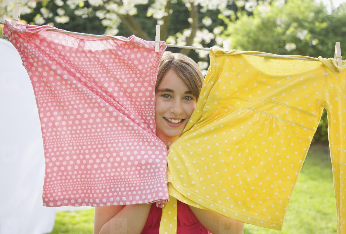 Smiling teenaged girl poking her face between two t shirts hanging from a clothesline